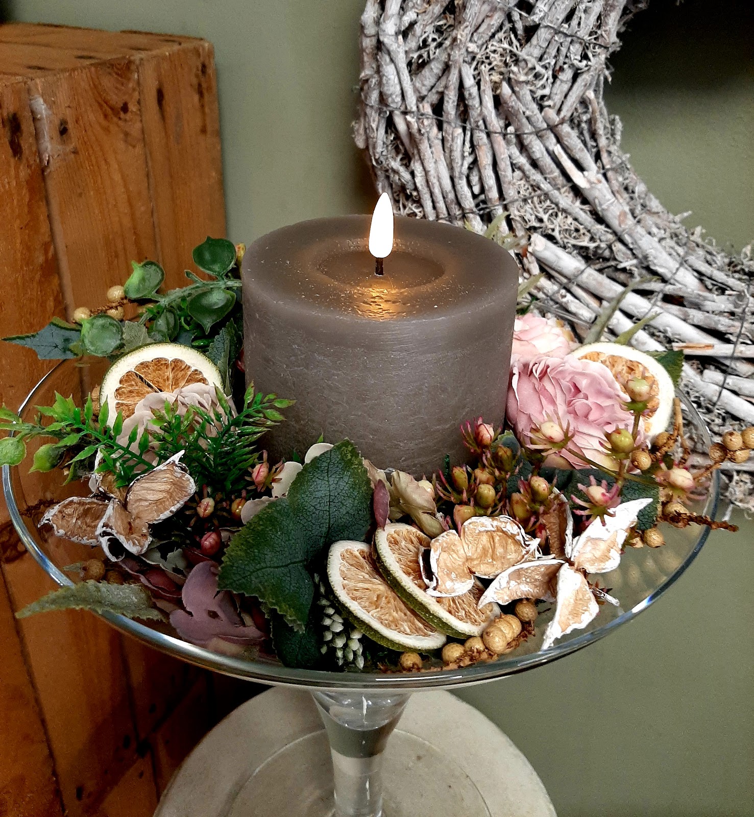 Kaarsarrangement in glasschaal met gedroogde citrus en rozen.